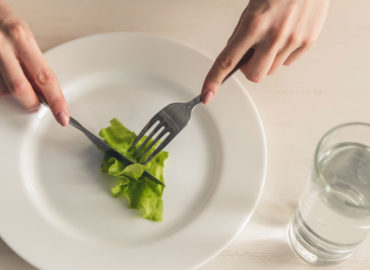 foto de um prato de comida, com uma folha de alface dentro, com garfo e faca prestes a cortá-la