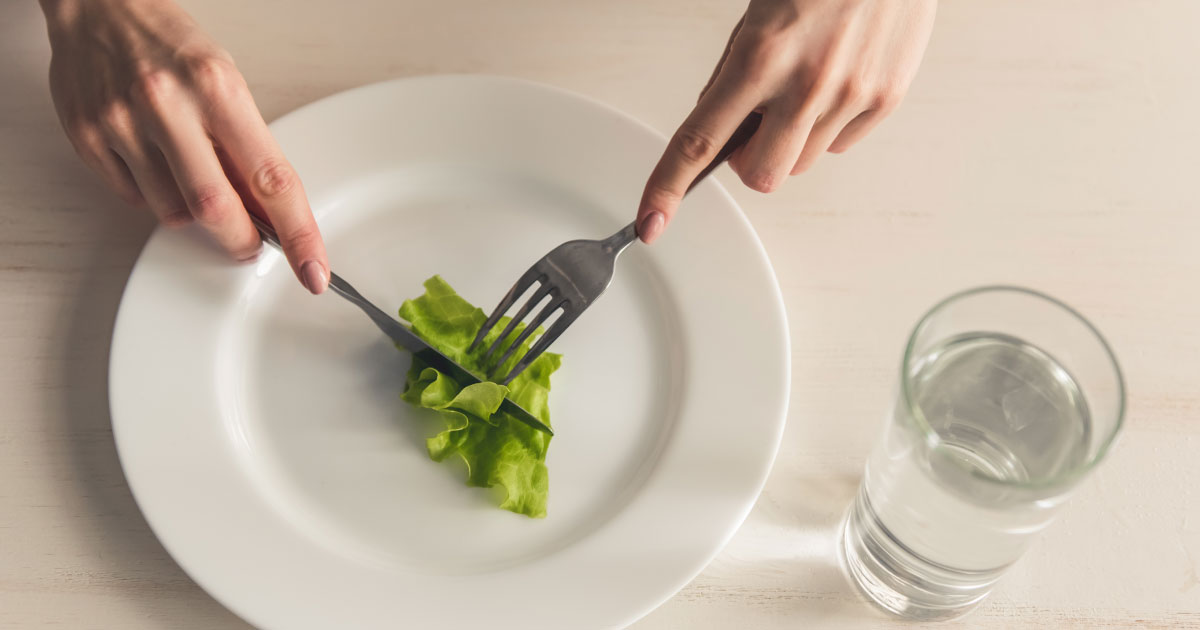 foto de um prato de comida, com uma folha de alface dentro, com garfo e faca prestes a cortá-la