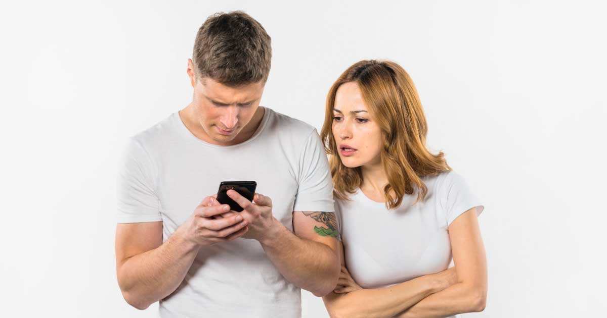 foto de um homem e uma mulher, lado a lado, o homem está mexendo em seu celular e a mulher está tentando ver o que ele está fazendo, demonstrando ciúme e curiosidade